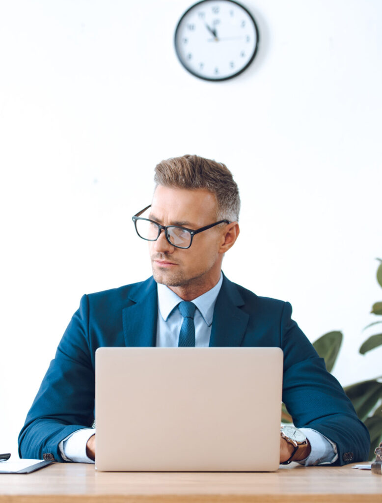 handsome lawyer in eyeglasses using laptop and looking away in office
